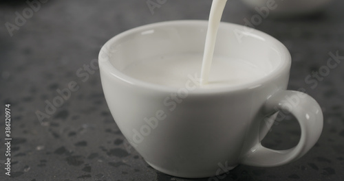 pour steamed milk into cappuccino cup on walnut table