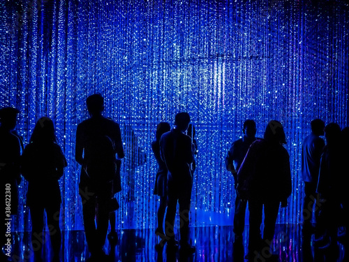Silhouettes of people standing in front of blue led light string