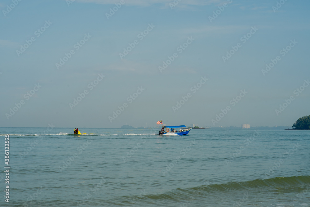 Boat with Malaysian flag is pulling children standing on the floating water raft in the sea.