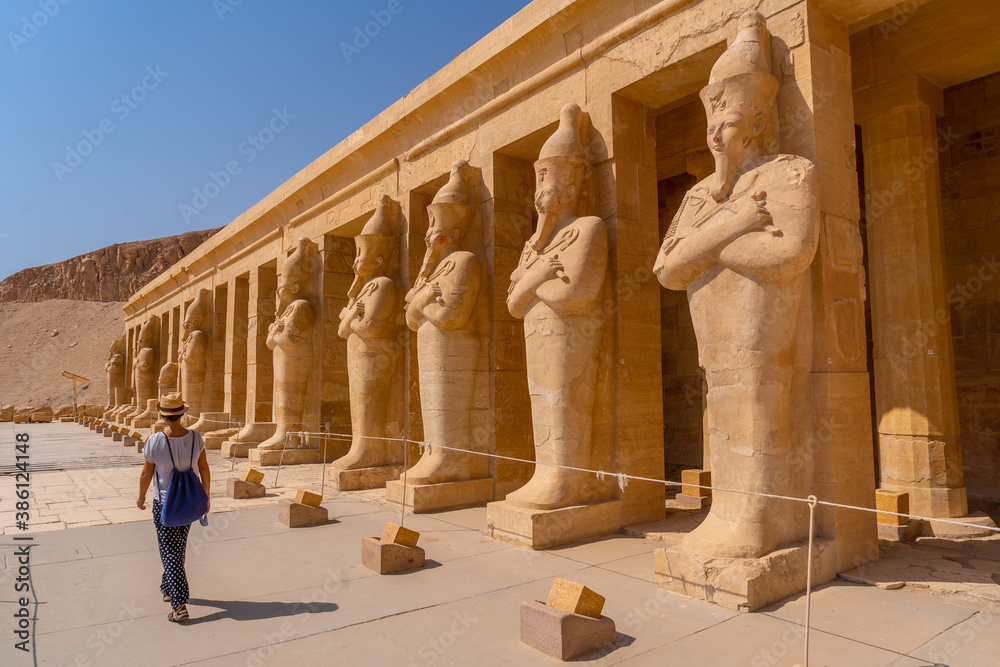 Fototapeta premium A young woman with pharaoh sculptures entering Hatshepsut's Funerary Temple in Luxor. Egypt