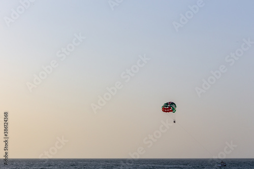 Parasailing in Dubai - single colorful parasail (parachute) tendem wing flying, towed behind a boat before sunset with orange and blue sky background. Copy space.