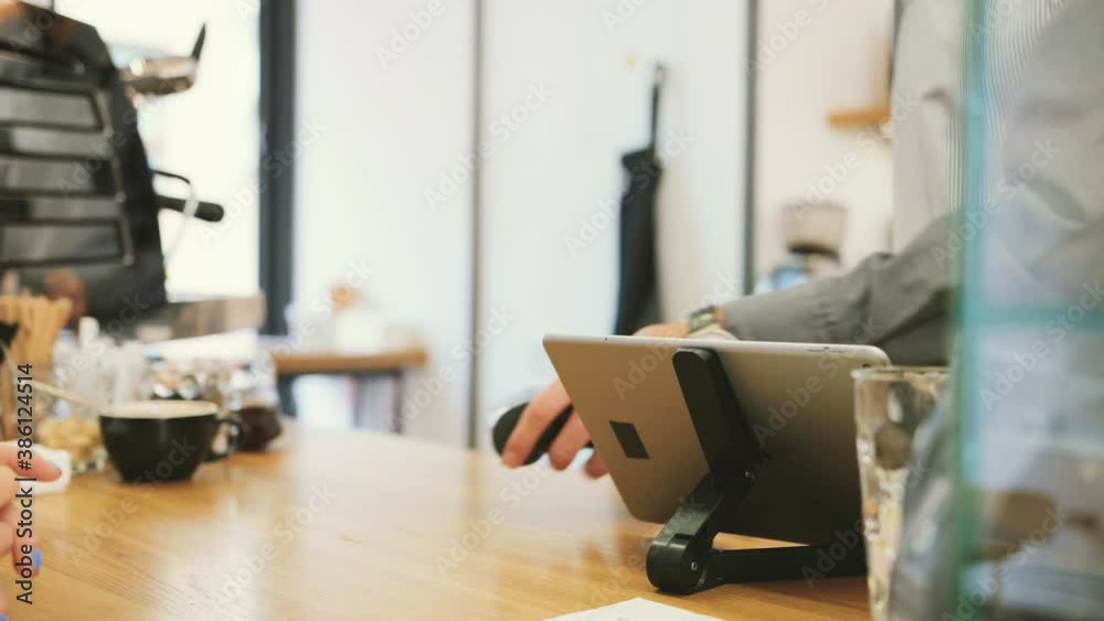 Close up of card payment in bank terminal. Digital tablet on light wood counter. Cashier serves client in cafe. Close up of card payment in bank terminal. Digital tablet on light wood counter. Cashier serves client in cafe.