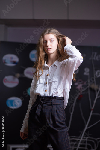 Young fair-haired girl model in a light shirt and trousers posing on a dark background.