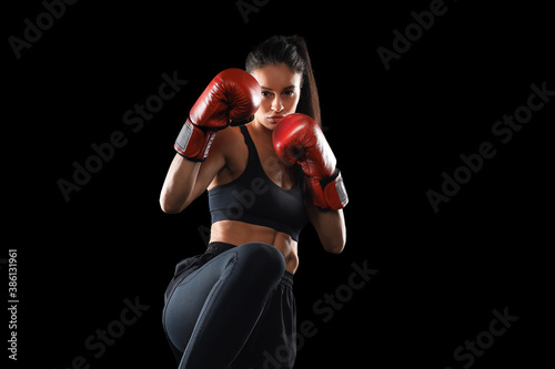 Kickboxing woman in activewear and red kickboxing gloves on black background performing a martial arts kick. Sport exercise, fitness workout.