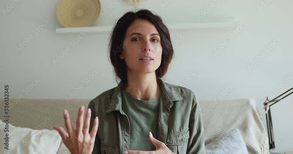 Head shot portrait woman sit on couch looks at web camera record new videoblog, makes a motivational speech, wave hand farewelling. Modern technology, promotional convincing video, influencing concept