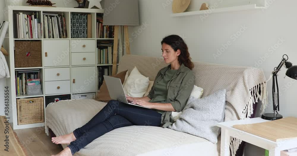 Relaxed woman sit on comfy sofa in cozy living room put computer on laps typing text, working remotely from home. Freelancer and telework activity, modern device and internet connection usage concept Relaxed woman sit on comfy sofa in cozy living room put computer on laps typing text, working remotely from home. Freelancer and telework activity, modern device and internet connection usage concept