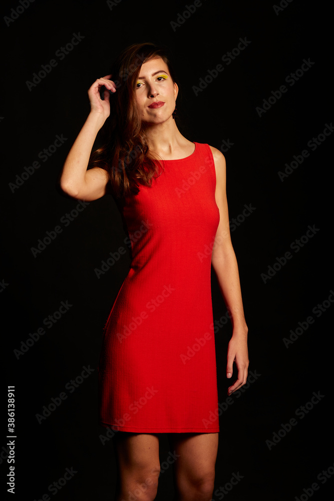 Young brunette Spanish woman dressed in sexy red dress, matching beaded earrings, and black shoes on black background,red Young brunette Spanish woman dressed in sexy red dress, matching beaded earrings, and black shoes on black background,red