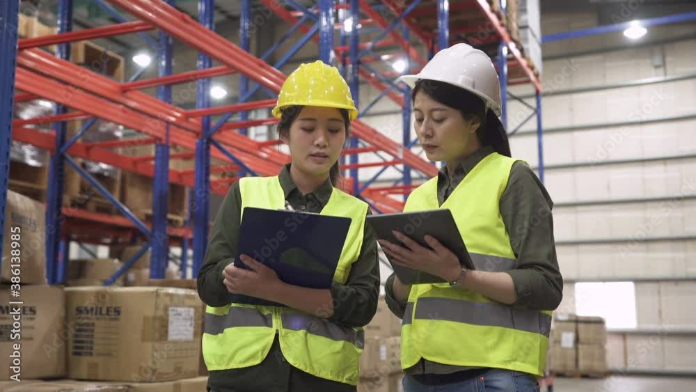 woman manager in white hard hat talking, showing tablet and training new girl employee in the factory warehouse woman manager in white hard hat talking, showing tablet and training new girl employee in the factory warehouse