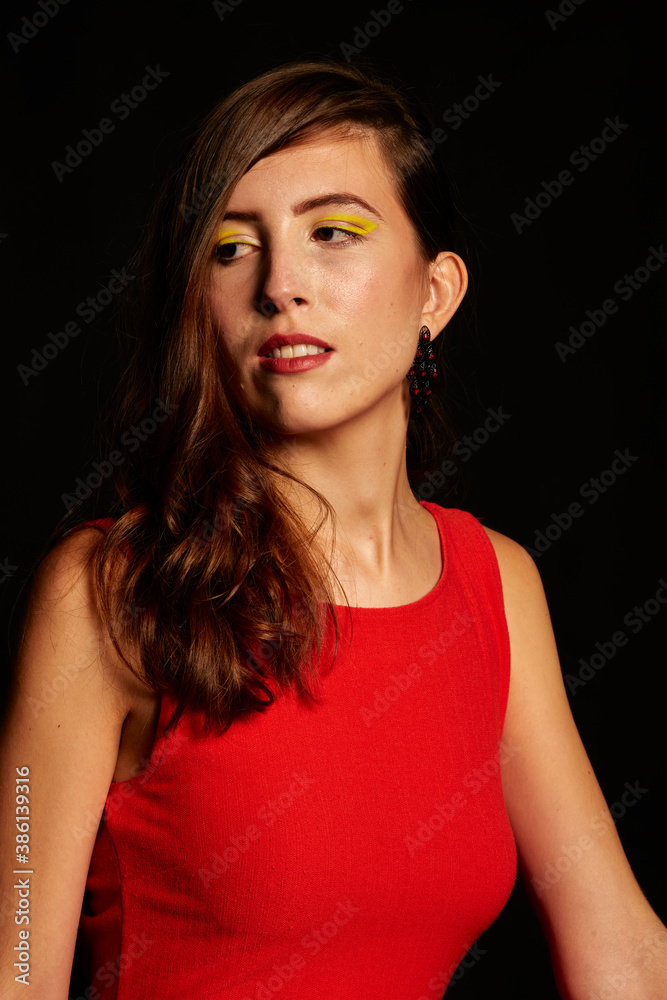 Young brunette Spanish woman dressed in sexy red dress, matching beaded earrings, and black shoes on black background,red Young brunette Spanish woman dressed in sexy red dress, matching beaded earrings, and black shoes on black background,red
