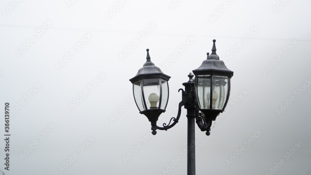 Top of a black street lamp and gray fog around, place for text. The concept of a cold wet summer morning