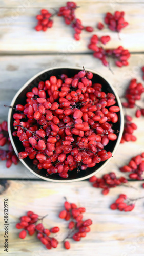 Berries and bunches of barberry in a bowl on a wooden surface. Barberry.