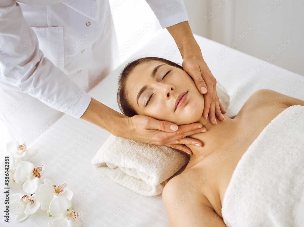 Beautiful brunette woman enjoying facial massage with closed eyes. Relaxing treatment in medicine and spa center concepts Beautiful brunette woman enjoying facial massage with closed eyes. Relaxing treatment in medicine and spa center concepts
