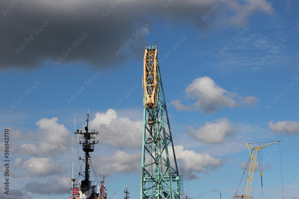 View from the water on the port water area with a crane of yellow turquoise color. Reflection in the water of the sky and faucet View from the water on the port water area with a crane of yellow turquoise color. Reflection in the water of the sky and faucet