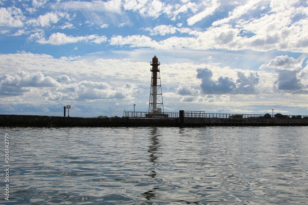 Signal beacon on the pier. Reflection of a beacon, sky and clouds in water. Baltic Sea