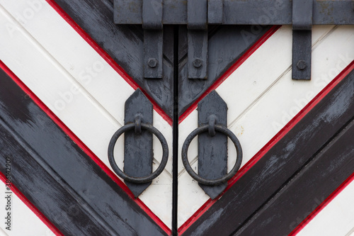 Fotografie Wrought iron door handles in the form of a ring and a steel bolt closed with a padlock on the gate in a medieval castle