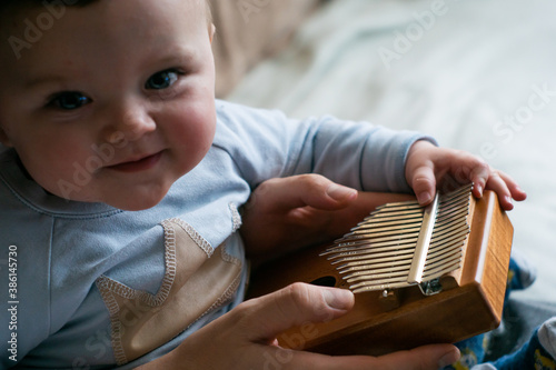 Spending time with family during lockdown - father teaches little cute baby boy how to play tiny instrument calimba. Selective focus on instrument. Baby smiling to the camera.