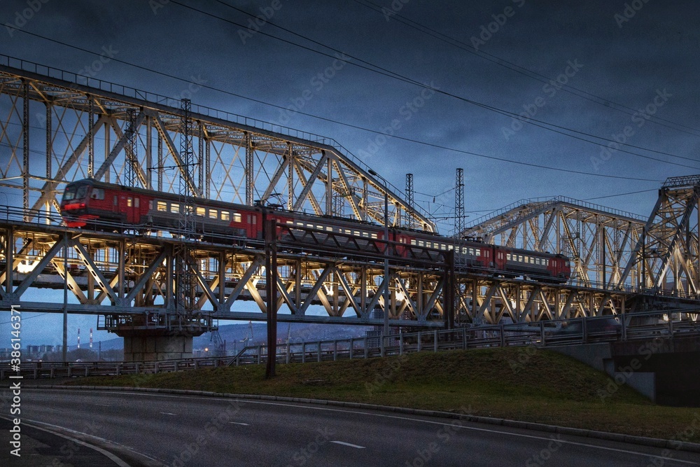 The Train moves at night on a lighted bridge over the river.