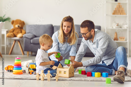 Mom, dad and baby playing at home with colored cubes sitting on the floor among colored toys.