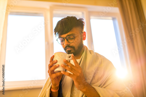 arabian indian man drinking hot lemon dinder masala tea in morning bedroom while feeling cold covered with a blanket photo