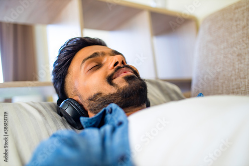 asian indian man living room lying on sofa closing his eyes and listening to music with a slight smile on face during a training session