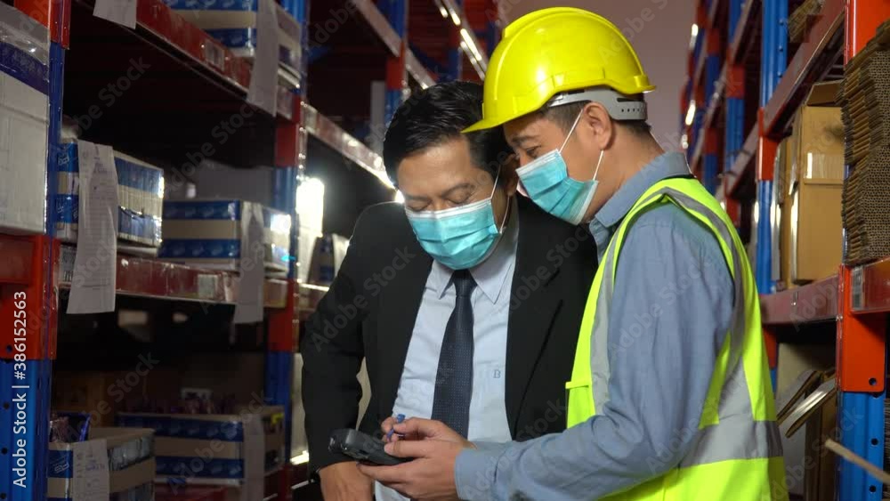 asian executive business man wearing face protective medical mask talking to warehouse manager in warehouse. Owner visits the factory and inspect with supervisor. coronavirus or covid-19 outbreak asian executive business man wearing face protective medical mask talking to warehouse manager in warehouse. Owner visits the factory and inspect with supervisor. coronavirus or covid-19 outbreak
