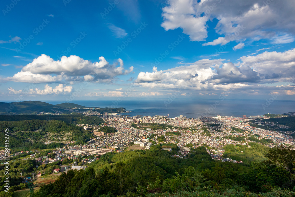 小樽山の展望台から見た、小樽の市街地とその奥にある石狩湾、雲の浮かぶ青空