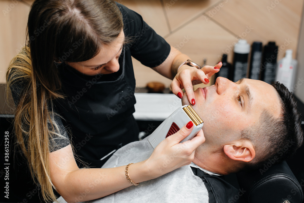 Fototapeta premium A professional stylist in a modern stylish barbershop shaves and cuts a young man's hair. Beauty salon, hair salon