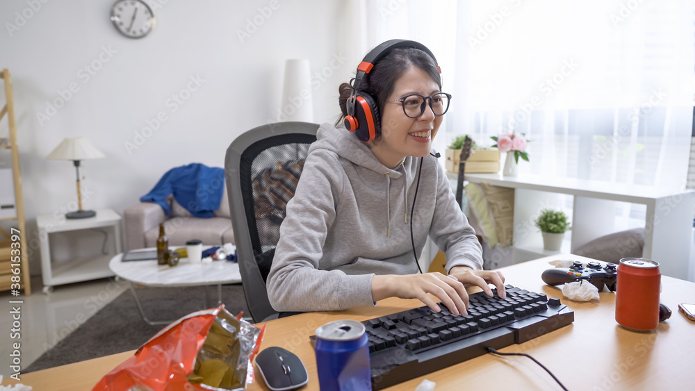 Happy asian japanese woman with headset playing online game on desktop computer at home on hot summer weather. young girl cheerful laughing typing on keyboard chatting with teammate before start.