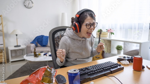 Fotografie, Obraz Pretty and excited asian gamer girl in headphones playing first-person shooter online video game on computer