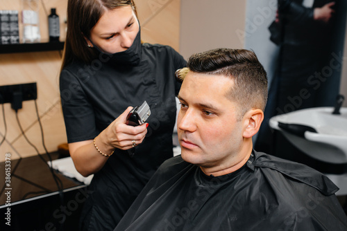 A professional stylist in a modern stylish barbershop shaves and cuts a young man's hair. Beauty salon, hair salon