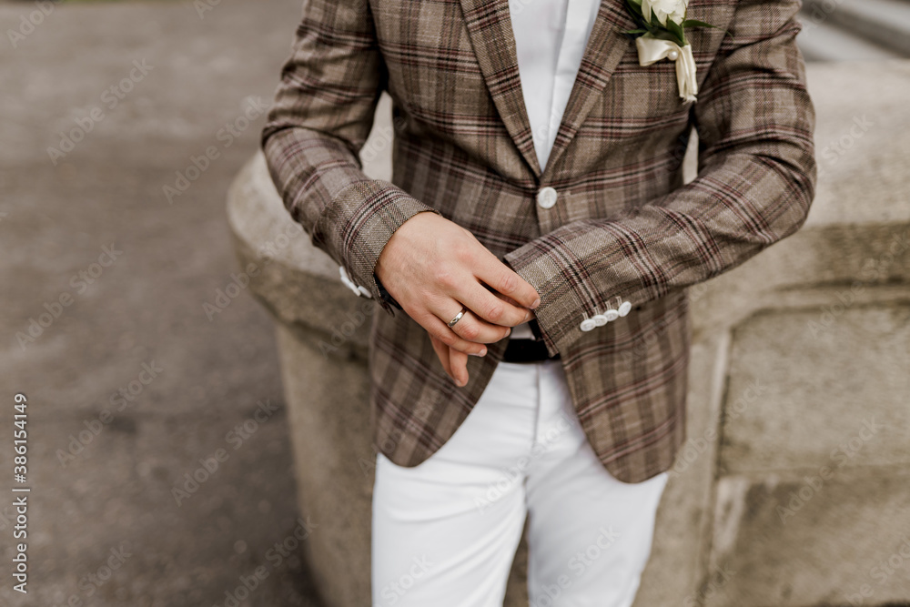 Groom in brown plaid jacket looks at his ring on the finger. Advert for wedding agency