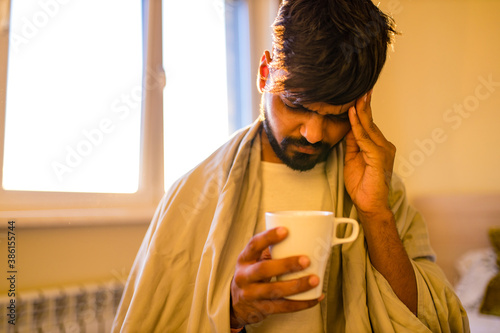 arabian indian man drinking hot lemon dinder masala tea in morning bedroom while feeling cold covered with a blanket photo