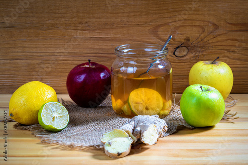 Cold homemade energy drink switchel in a mason jar next to apples, ginger and lemon on a wooden table photo