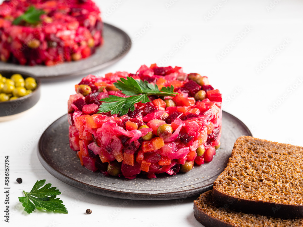 Vinaigrette. Traditional russian beetroot salad with boiled vegetables, pickled cucumbers, sour cabbage, olive oil and green canned peas. Vegetarian healthy dinner. White wooden background. Close up.