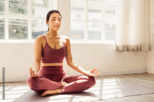Young attractive smiling woman practicing yoga, sitting in Half Lotus exercise at home. Concept of healthy life and natural balance between body and mental development. Full length