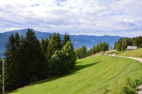 South Tirol in Italy, hiking area around the municipality of Percha near the town of Bruneck, mountain range on horizon, meadow and forest, a hiking trail on the right, sunny day in autumn, cloudy sky