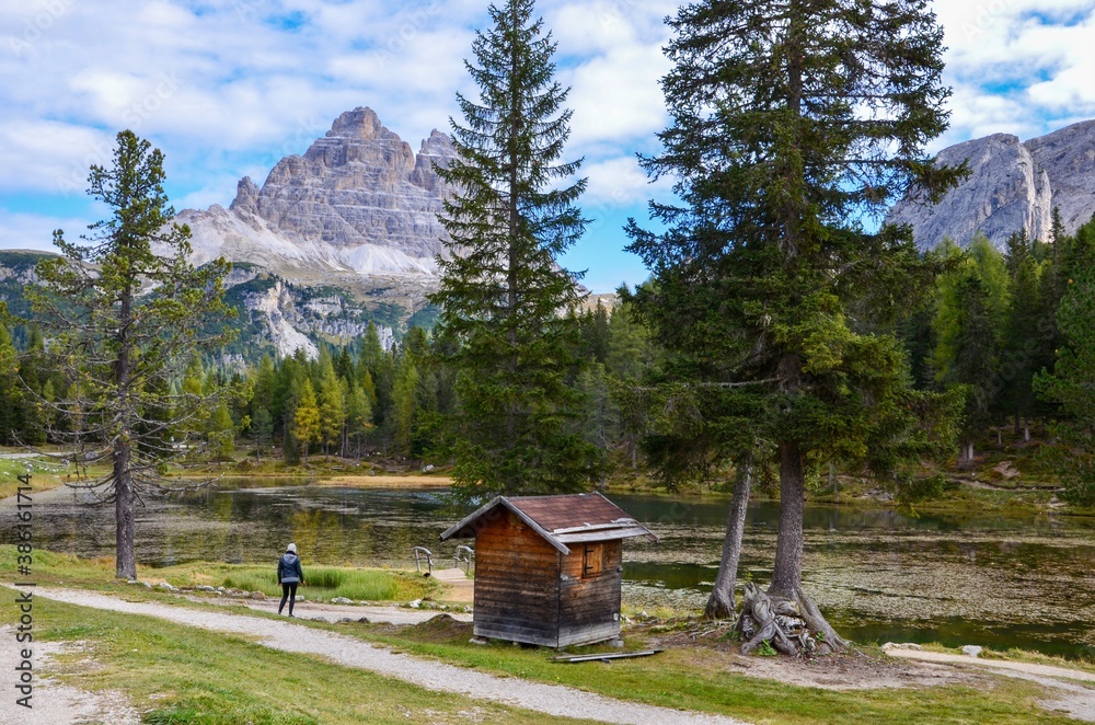 Tre Cime (Three Peaks) di Lavaredo Natural Park, Dolomites mountains, South Tirol, Italy, a lake in front, autumn landscape, a woman on a hiking trail, blue sky with clouds background, a sunny day Tre Cime (Three Peaks) di Lavaredo Natural Park, Dolomites mountains, South Tirol, Italy, a lake in front, autumn landscape, a woman on a hiking trail, blue sky with clouds background, a sunny day