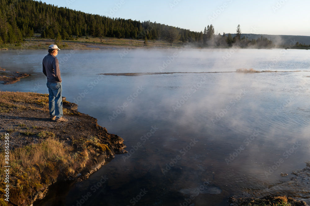 Lone visitor standing on the shore of a thermal lake watching the steam rising, Fire Hole Lake, Yellowstone NP, Wyoming