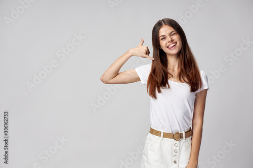 A woman holds two fingers near her face and winks on a light background imitating a phone message 