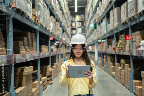 Female warehouse worker inspecting a warehouse in a factory. Wear a safety helmet and glasses for work safety. Concept of warehouse.