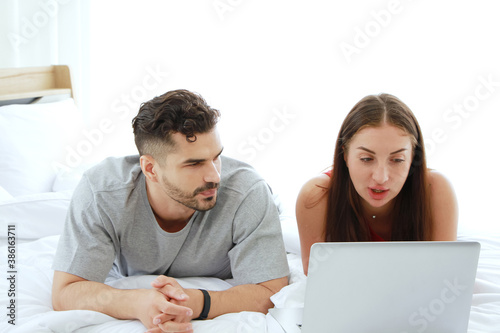 Young Caucasian couple love is relaxing with laptop in social media for shopping online in bedroom. Technology for Married family lifestyle on holiday Concept. © cocorattanakorn