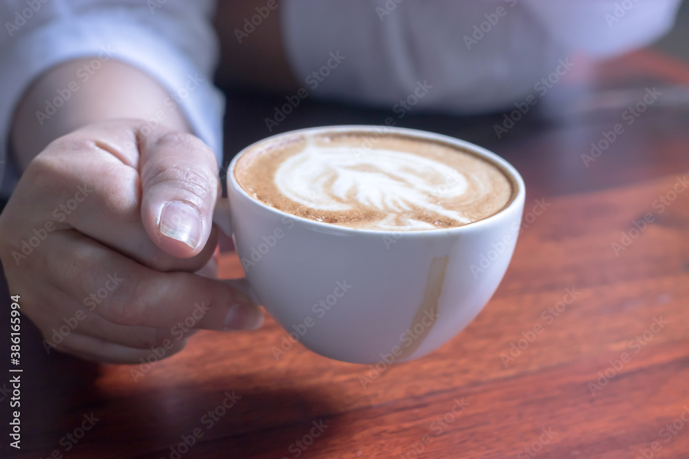 Fototapeta Morning coffee in a white cup in the hand of a girl on a wooden table in the cafe