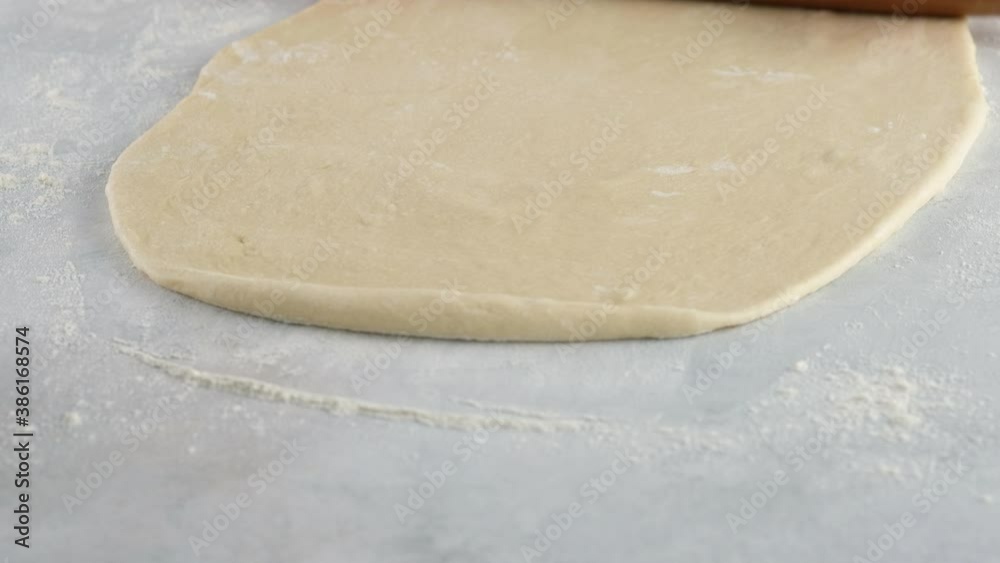 Cook rolls the dough with a rolling pin, shaping the dough. Female hands kneading dough in flour on the table. Close up. Production of cinnamon rolls. Bakery products. Cook rolls the dough with a rolling pin, shaping the dough. Female hands kneading dough in flour on the table. Close up. Production of cinnamon rolls. Bakery products.