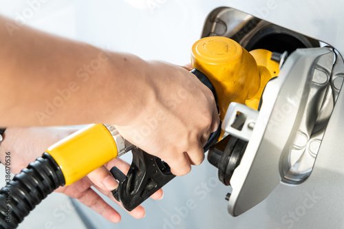 Hand holding yellow color nozzle to refuel vehicle at gas station
