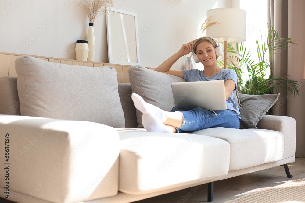 Smiling young woman with headphones and laptop on the sofa. Smiling young woman with headphones and laptop on the sofa.
