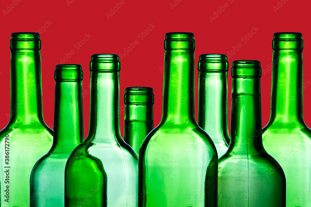 Green wine bottle. Empty glass isolated on red. Set of blank no label wine bottle in a row. Winery shelf texture. Alcohol background. Shiny transparent vibrant color panoramic view. Green wine bottle. Empty glass isolated on red. Set of blank no label wine bottle in a row. Winery shelf texture. Alcohol background. Shiny transparent vibrant color panoramic view.