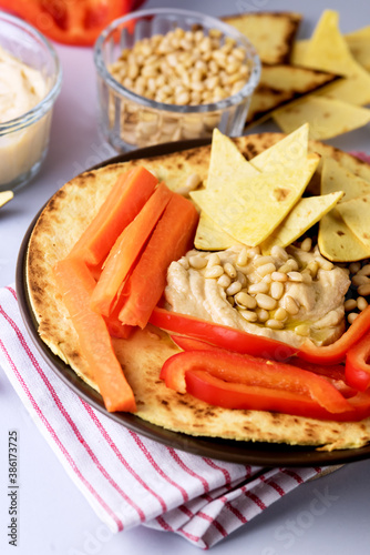 Plate of Hummus Chickpea Dip Nuts Paprika Carrots and Olive Oil With Pita or Chips Blue Background Horizontal