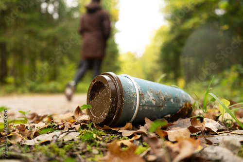 Old disposable coffee cup in the forest next to the road with person in a background. Plastic recycling, pollution and global warming theme. Take away food industries impact on the environments. 