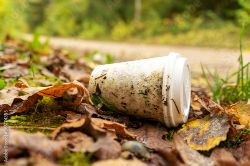 Old disposable coffee cup in the forest next to the road. Plastic recycling, pollution and global warming theme. Take away food industries impact on the environments. 