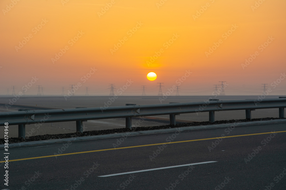Sunrise over the United Arab Emirates with the silhouettes of the transmission towers at the horizon seen from the highway between Abu Dhabi and Liwa Oasis